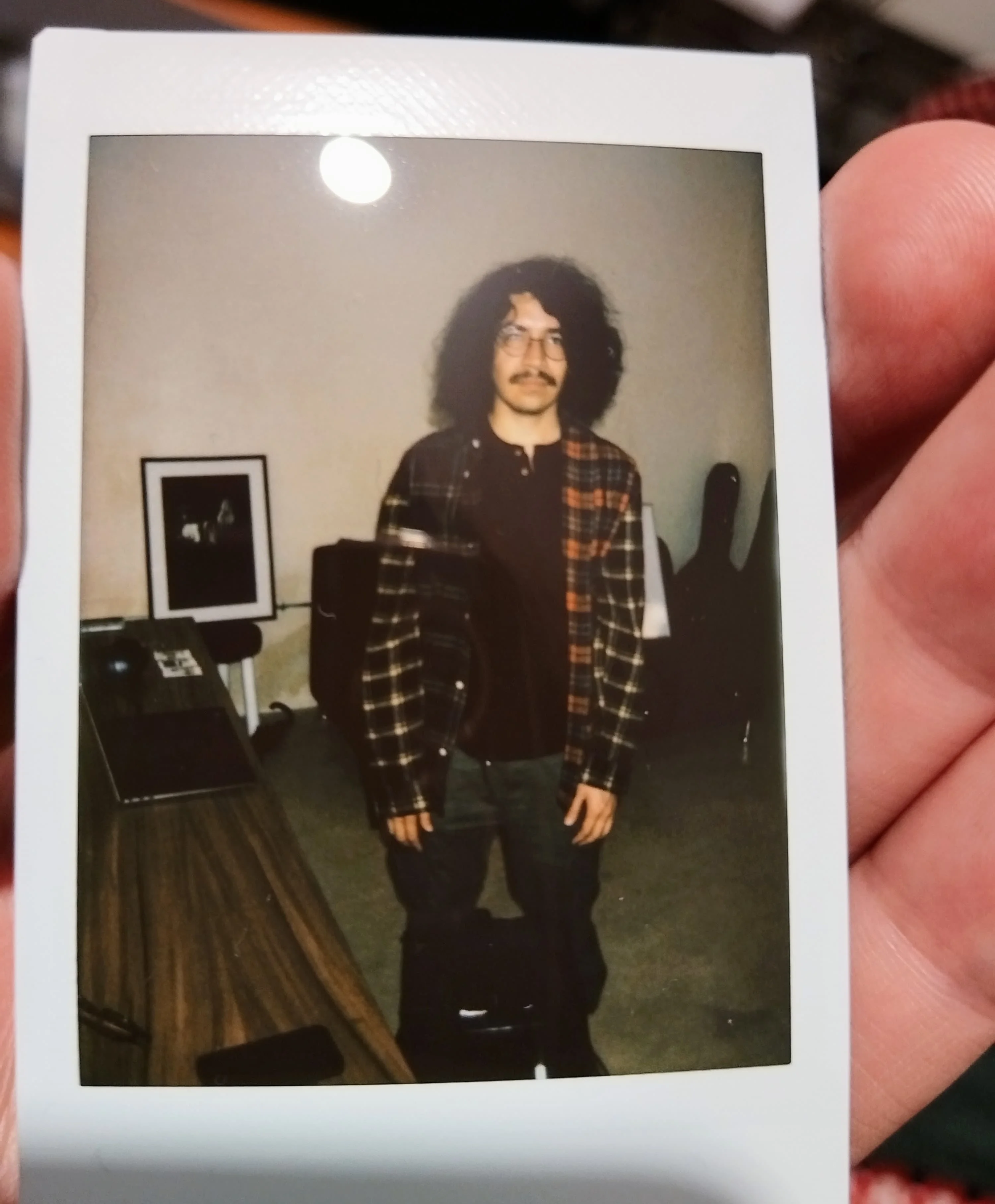 Óscar A. Montiel standing in a room, in an instant photo held in a hand.
